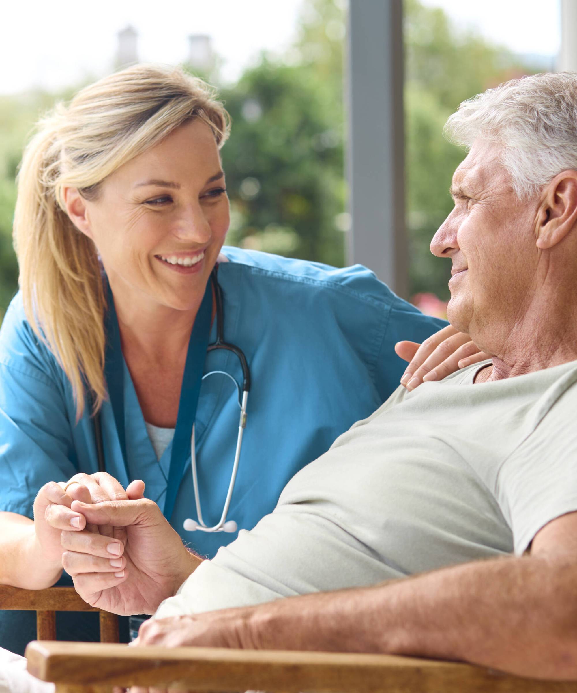 Female Nurse Comforting Depressed Senior Man Sitting In Chair On Home Visit